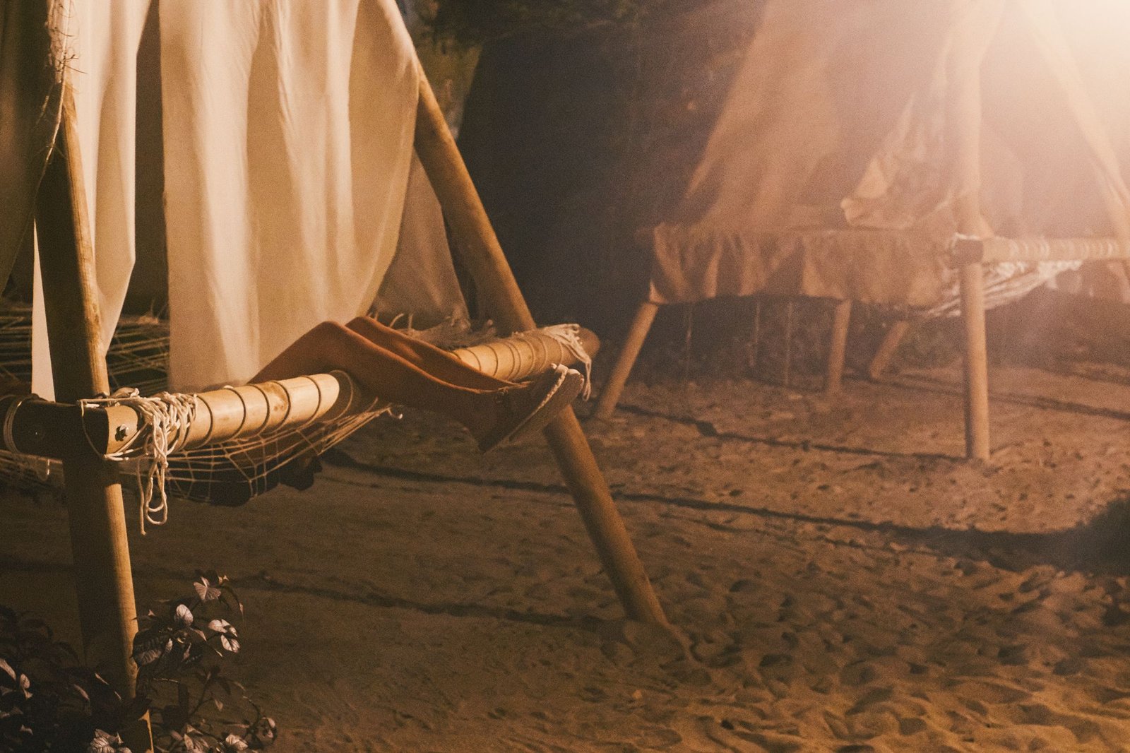 Legs stretched out on a hammock bed on the sand, white canopies glowing in the night light
