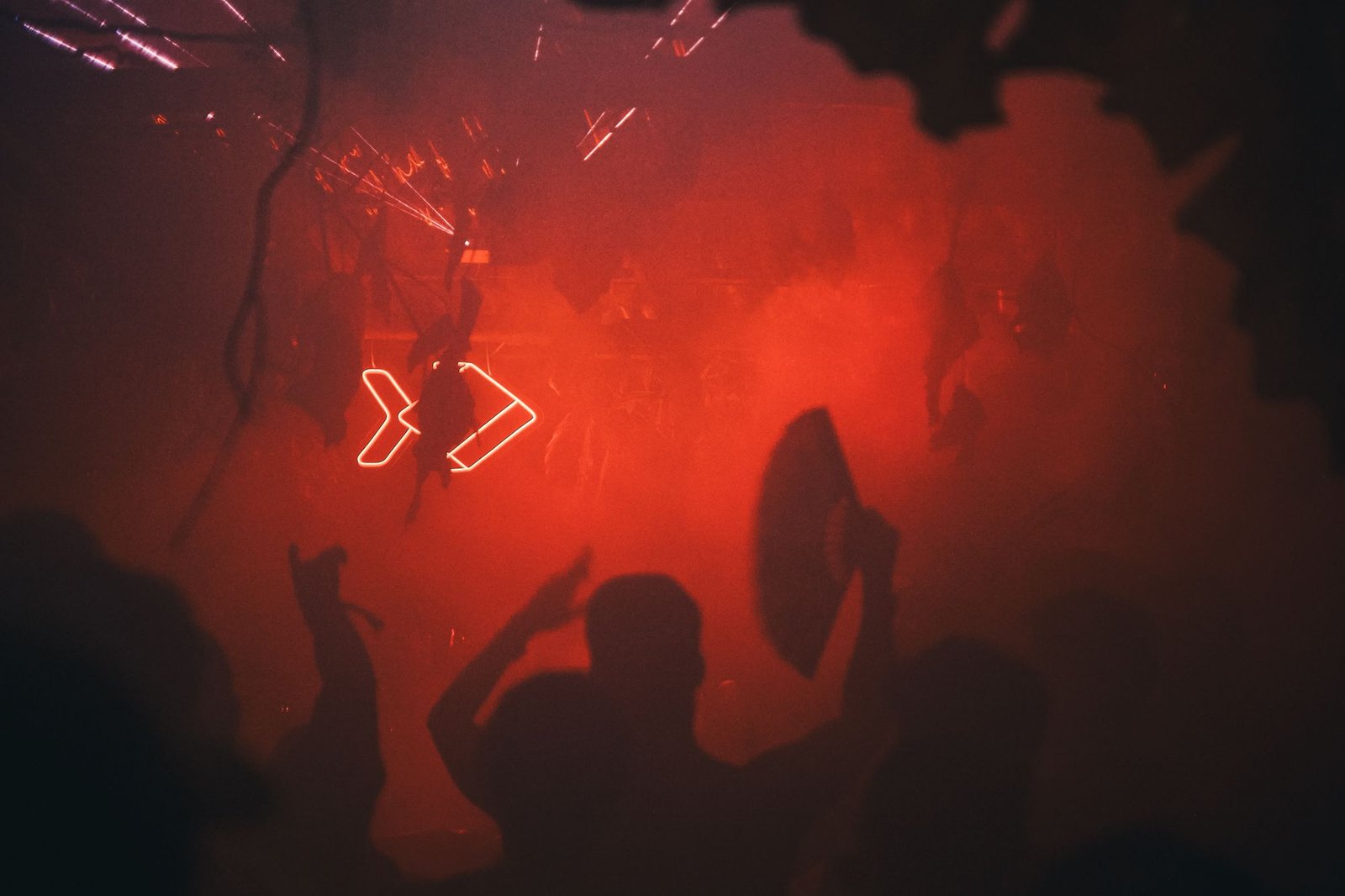 The dancefloor in red light and smoke, a neon sign through the leaves and a fan raised in the crowd